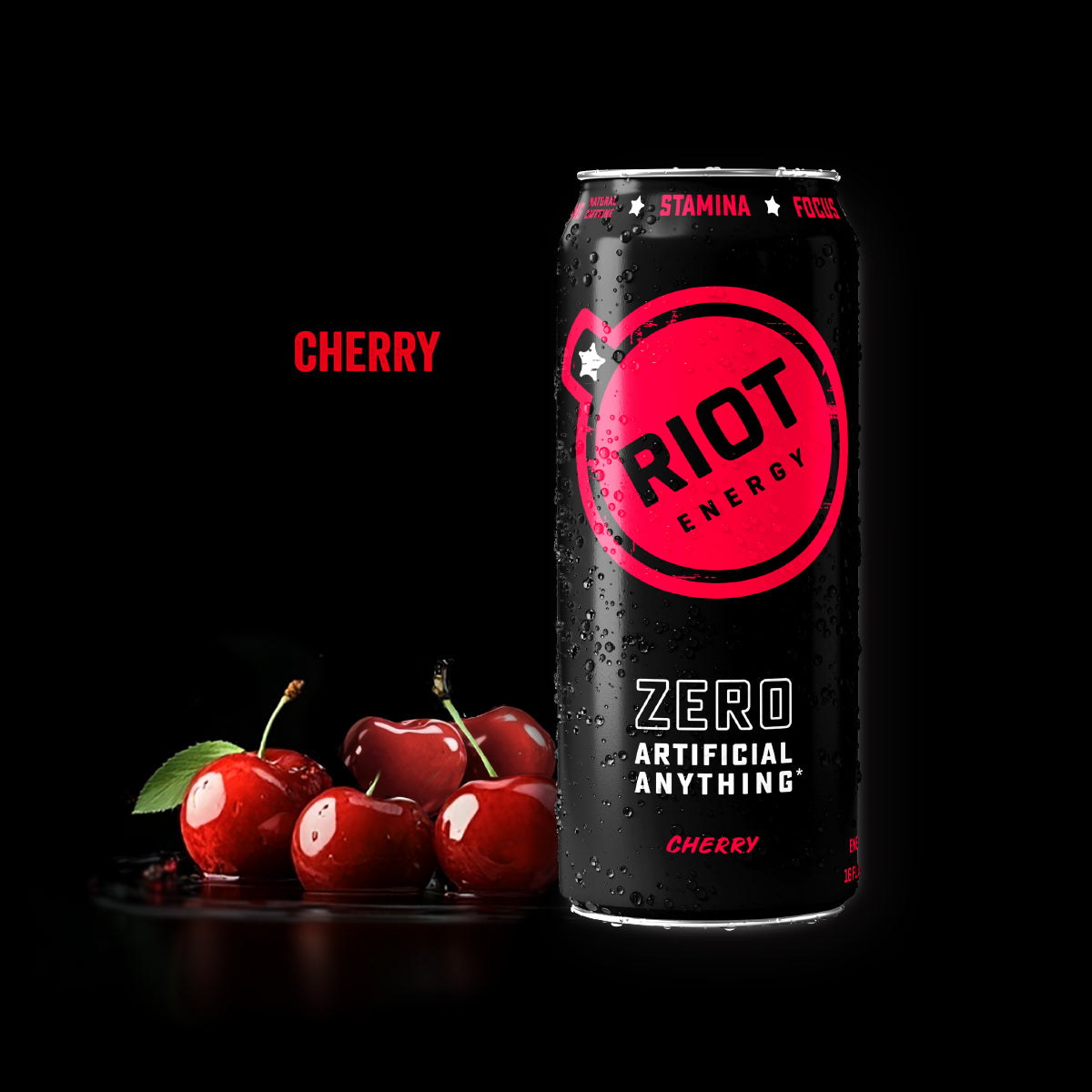 A can of Riot Cherry Energy Drink. On the can reads: "Zero Artificial Anything Cherry" and the word Cherry in red, shown next to fresh red cherries on a black background with the word 'CHERRY' in red text.